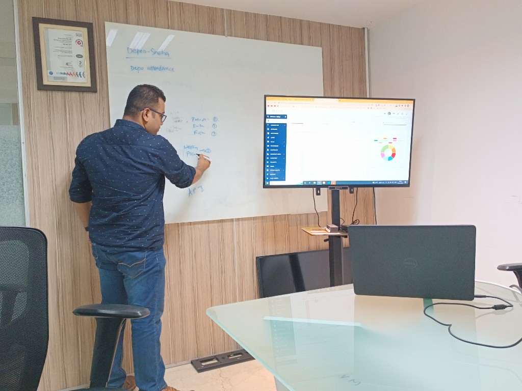 Naffys Mir at a whiteboard beside a large screen showing charts and product metrics.